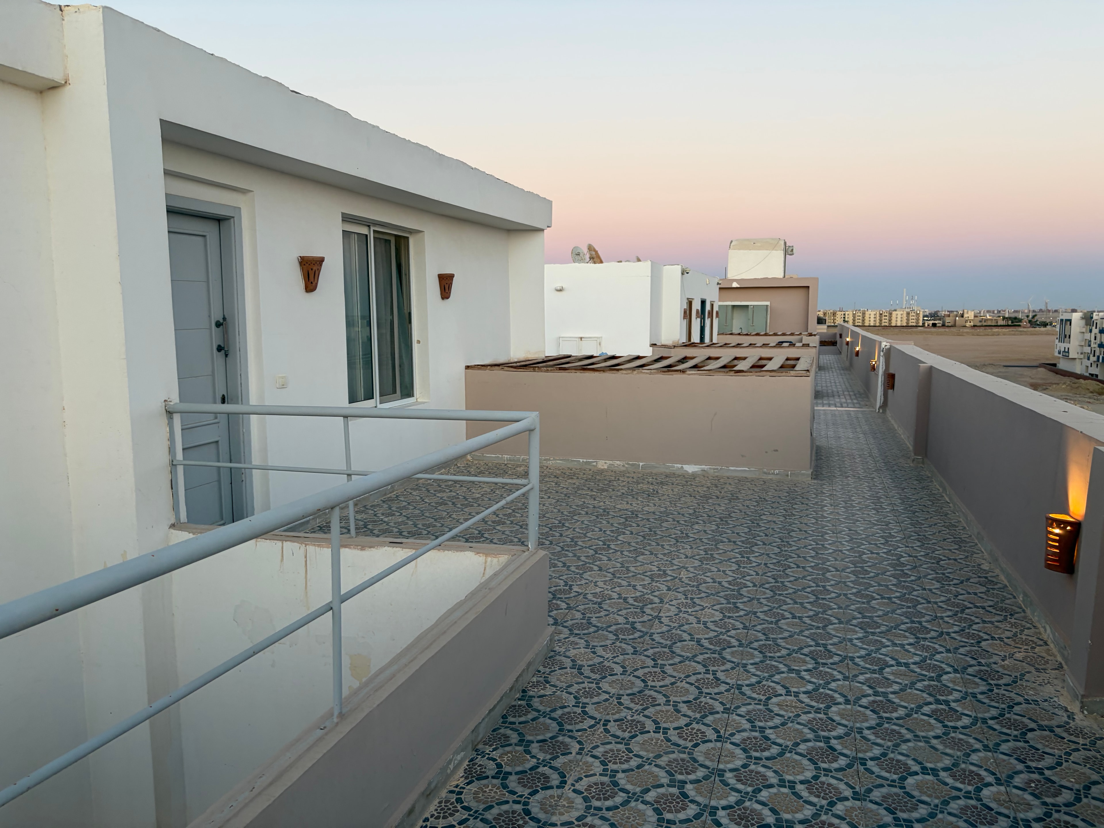 Wider view of illegal rooftop villas — sliding doors, windows, metal balustrade railings and pergola structure occupying the communal relaxation space