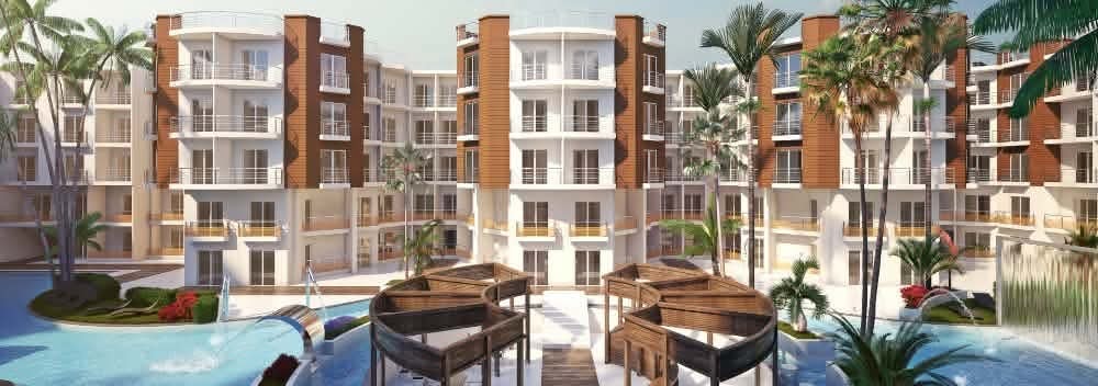 Brochure render — sweeping pool complex with circular timber cabana structures, palm trees, water features and full resort facade