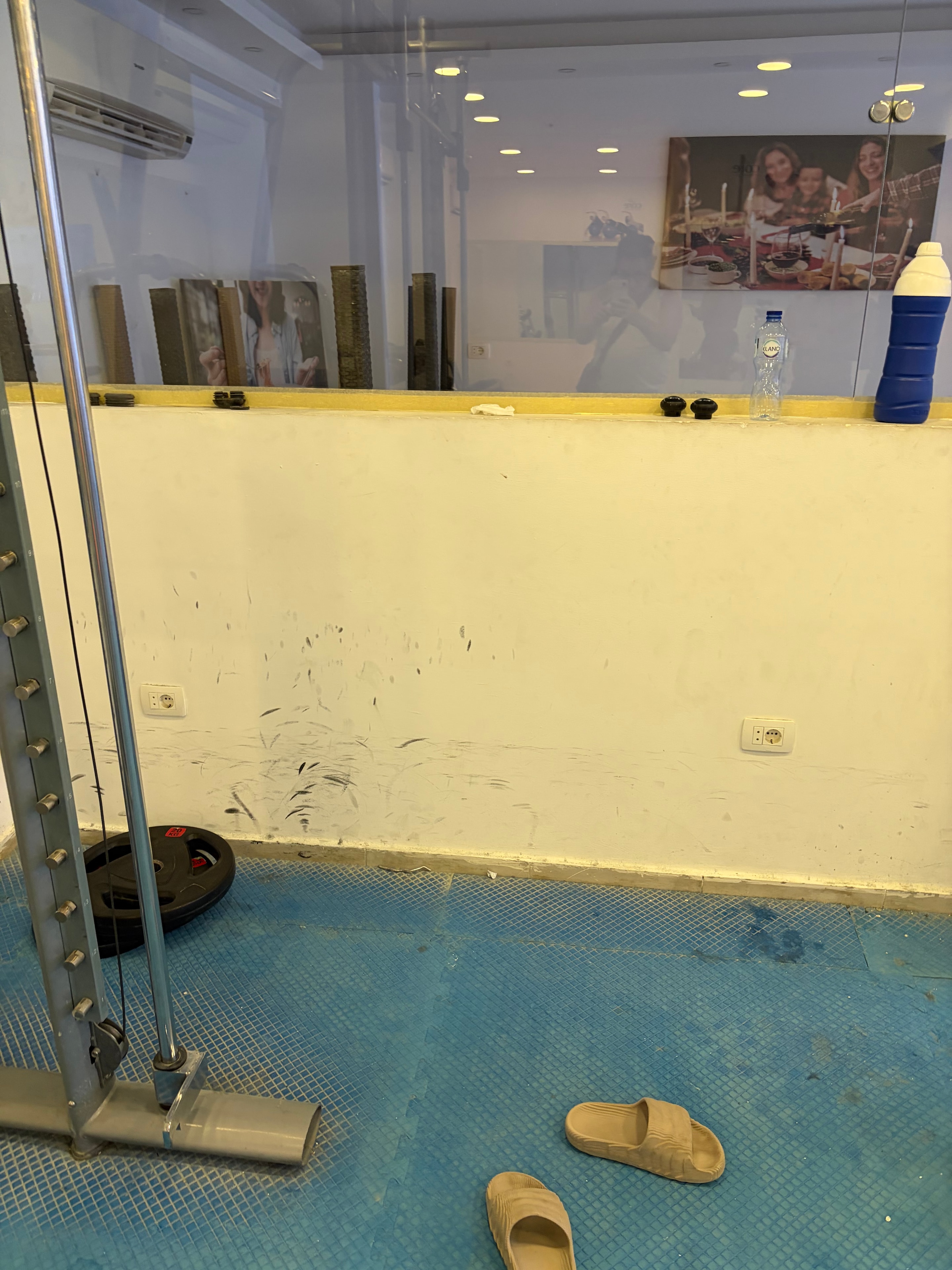 Mirror selfie showing the full tiny sparse gym space with minimal equipment