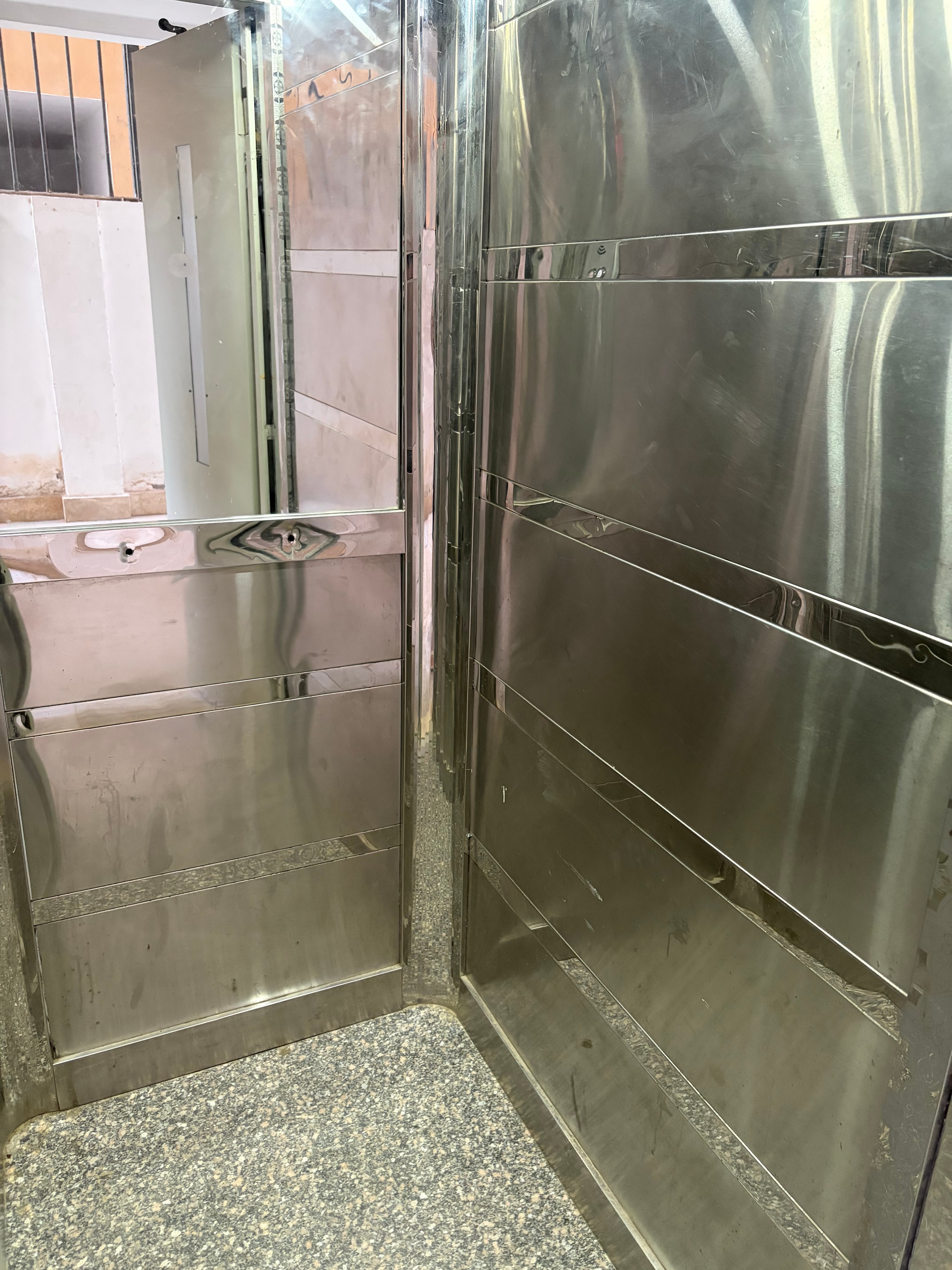 Lift interior looking out through door gap — landing clearly visible through open shaft void