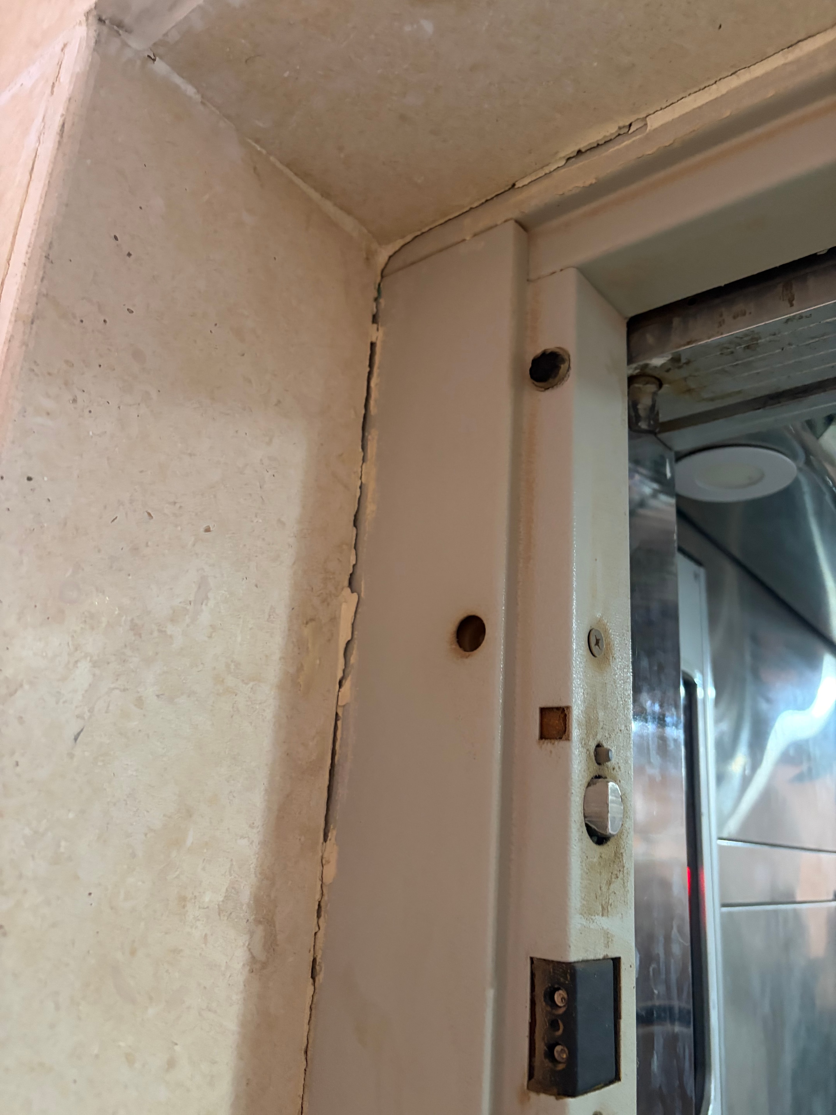 Door sill close-up — cracked crumbling concrete threshold, missing bolt holes, corroded safety interlock