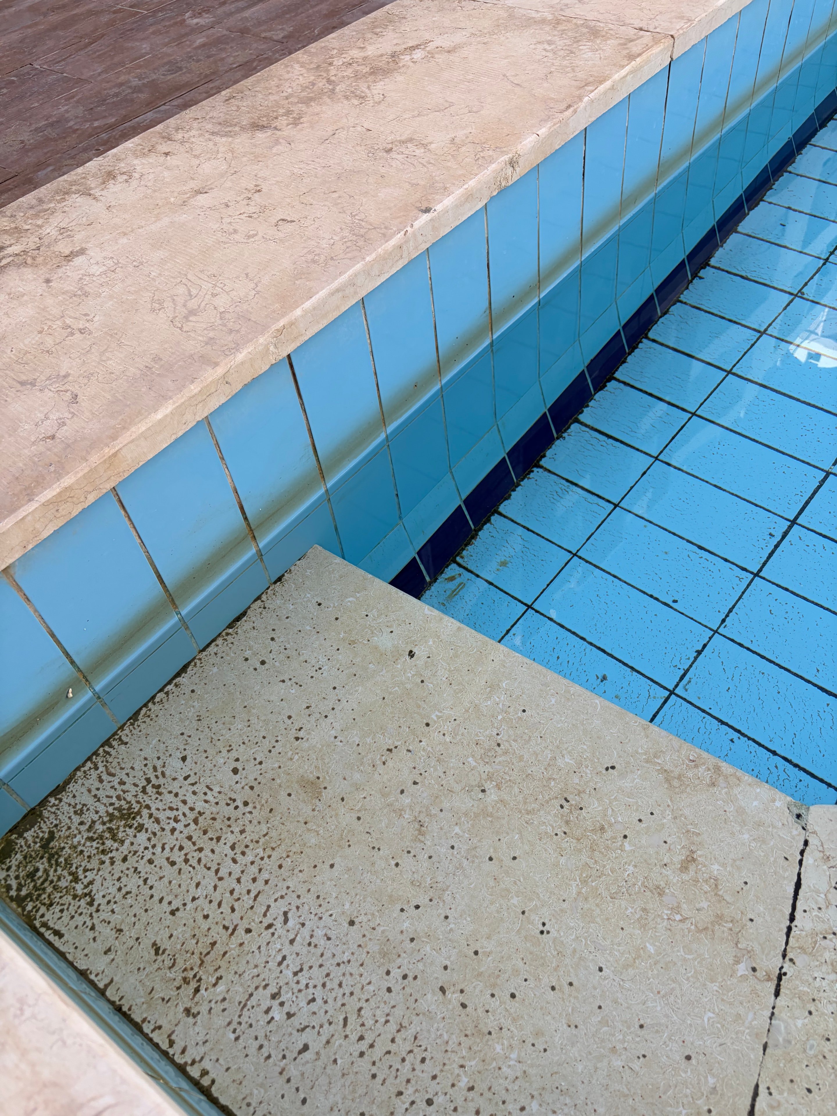 Sun lounger frame close-up — white plastic heavily soiled, RUBEX INTERNATIONAL MADE IN EGYPT stamp visible, dark mismatched tiles behind