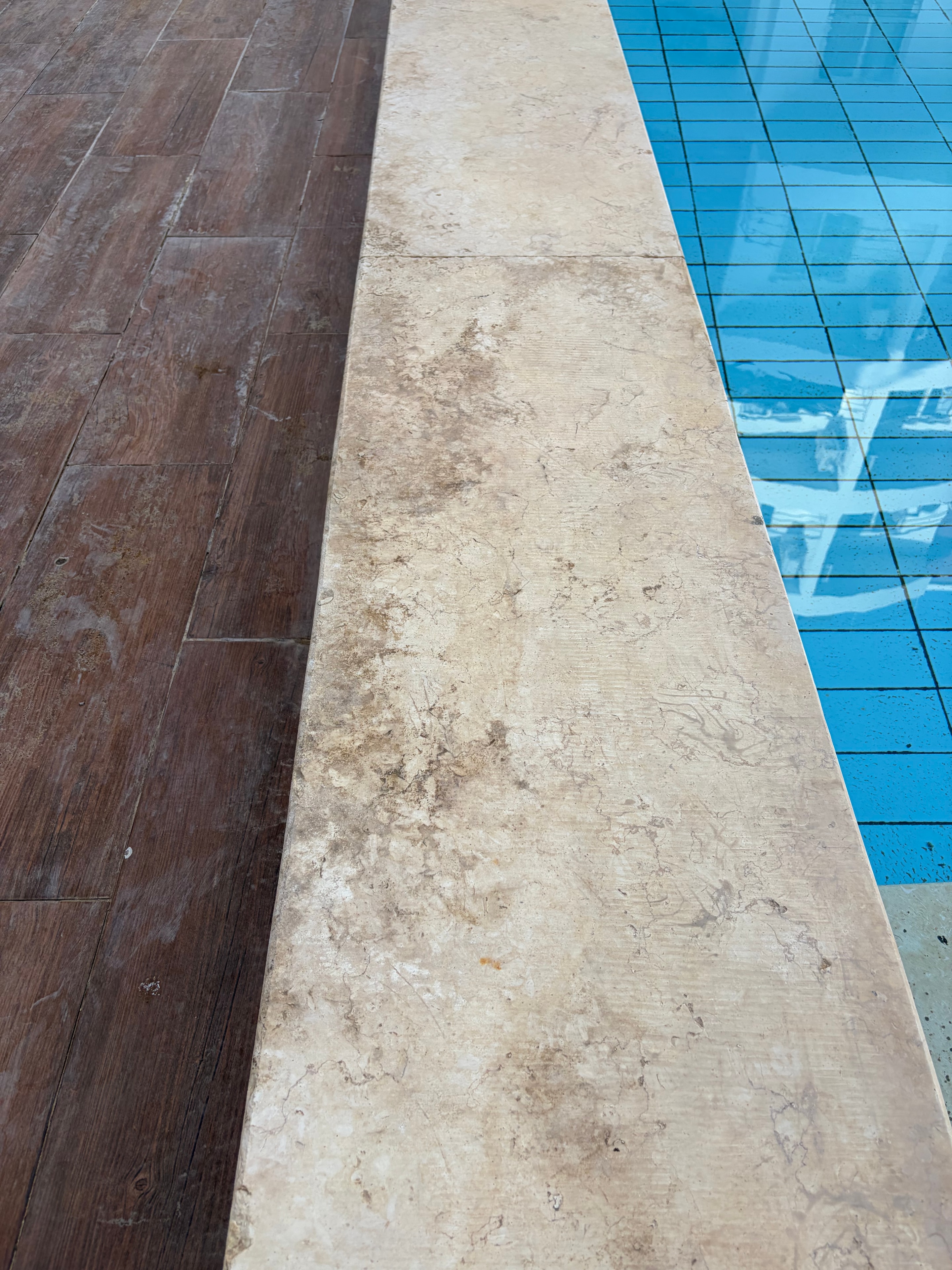 Pool seating alcove — built-in stone bench with mismatched wood-effect tiles on back wall, debris accumulated in corners