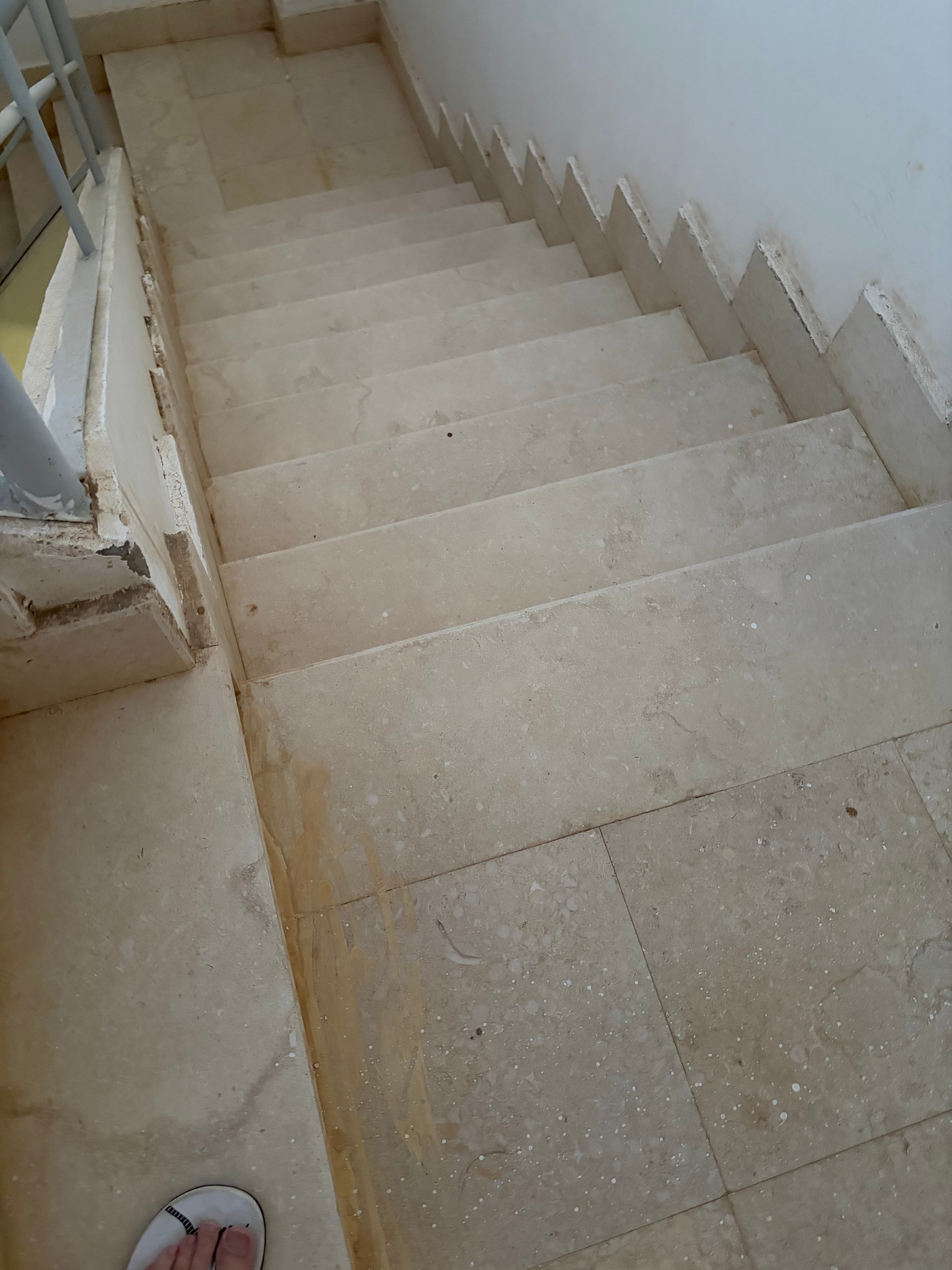 Unfinished floor area — bare brown screed with no tiles laid, window frames set into the floor level, abandoned ceramic piece, white adhesive blobs — never completed