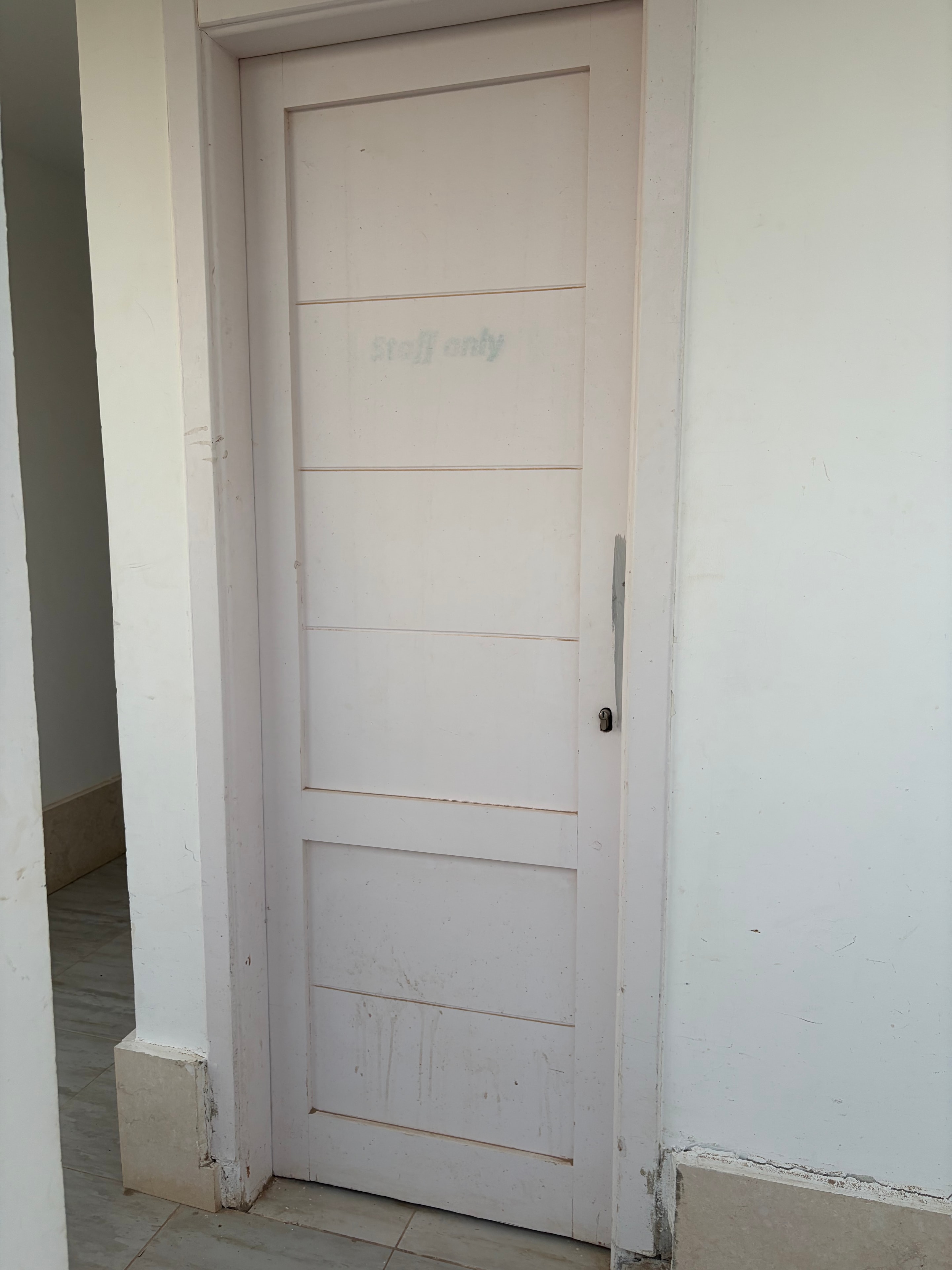 Graffiti on communal shutter panel — "Aqua Palms" written in marker on the white panelled door of a communal service room, bare concrete block surround with no finishing