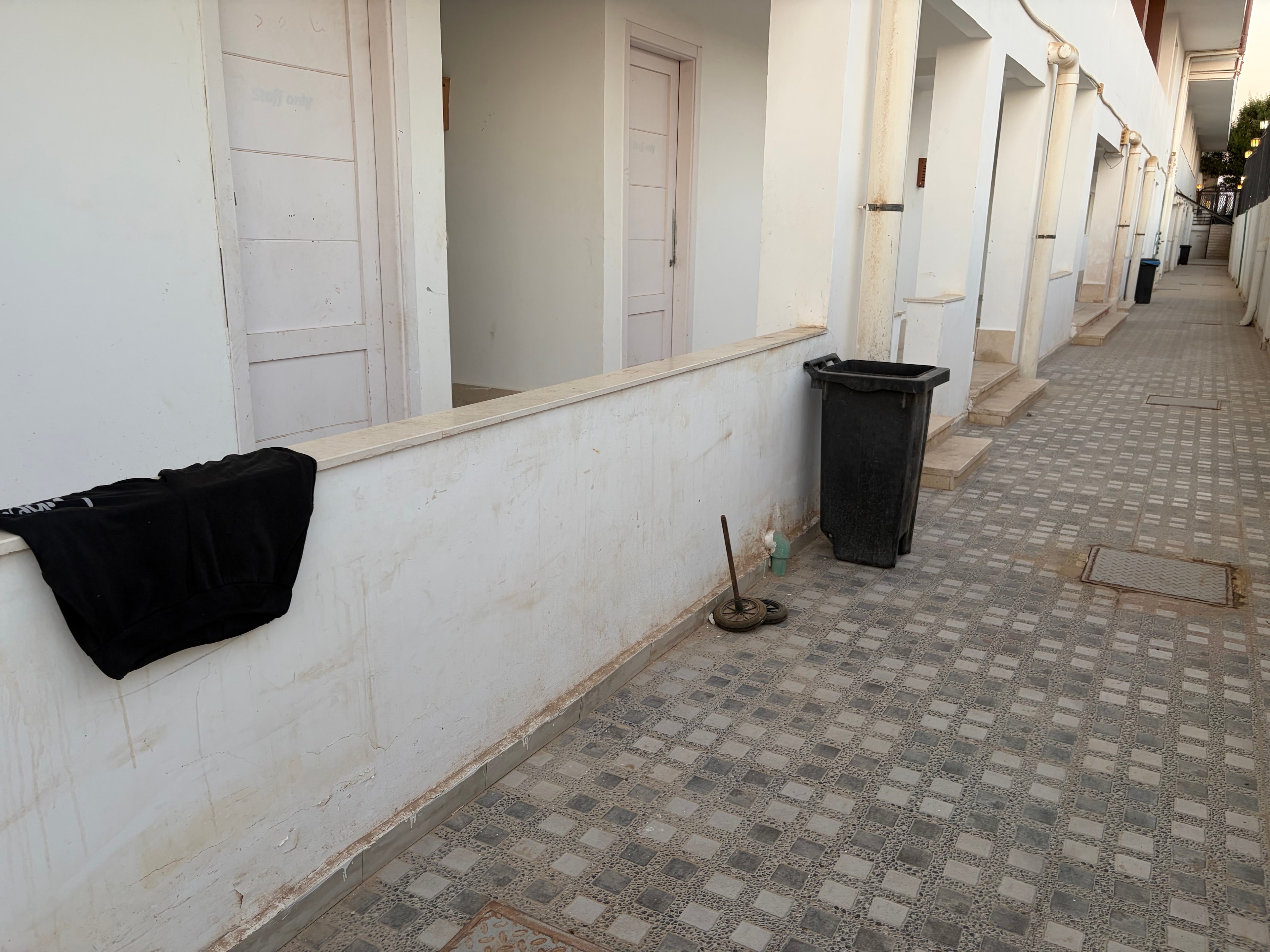 Communal corridor with deteriorating ceiling and covered speakers — heavily stained decorative tile ceiling, black speaker units covered in fabric bags, exposed pipework along the wall