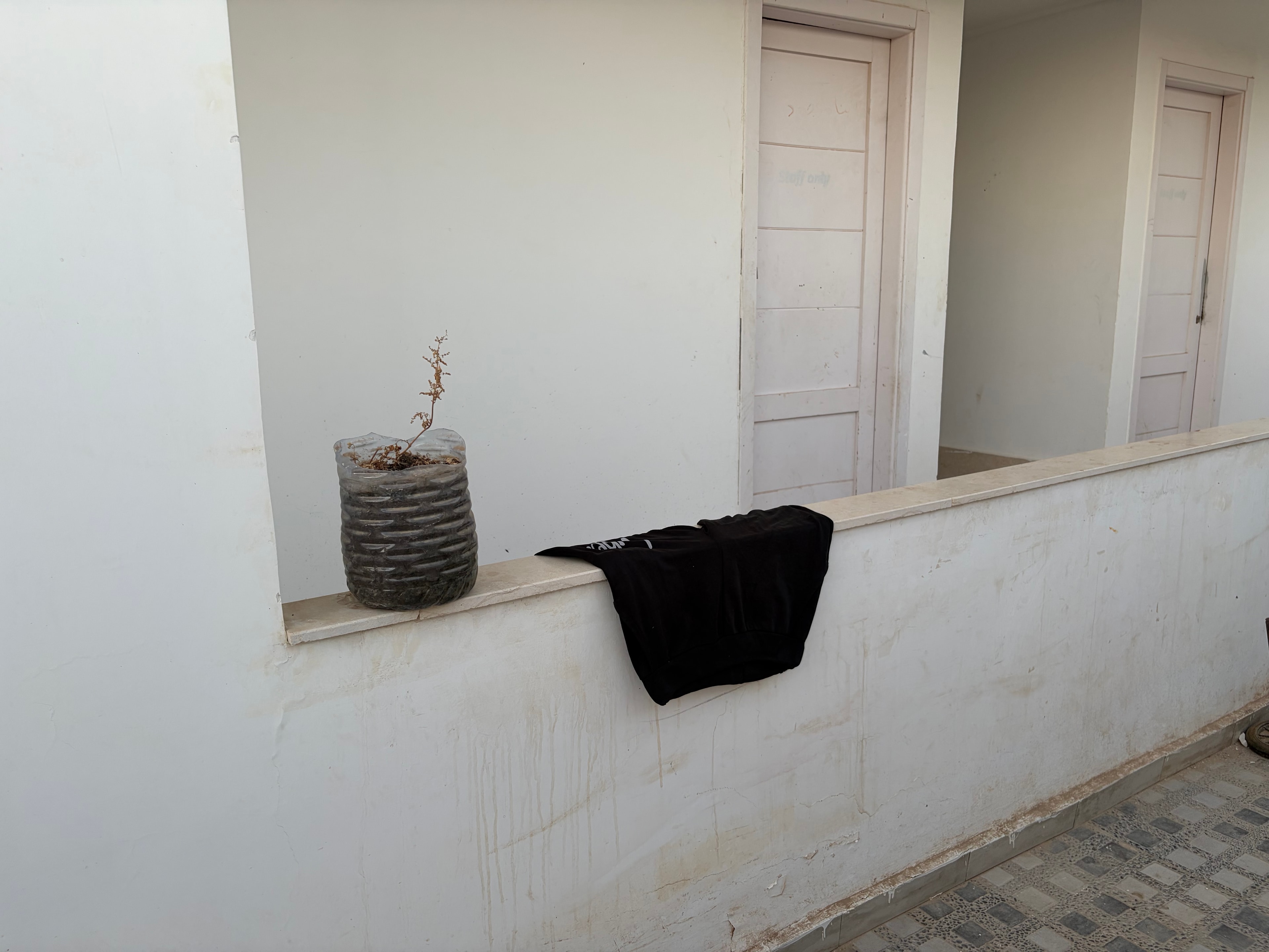 Close-up of covered speaker and loose drain pipe — black fabric-covered speaker unit beside a corrugated waste pipe hanging loose from the wall with dead plant matter dangling from it