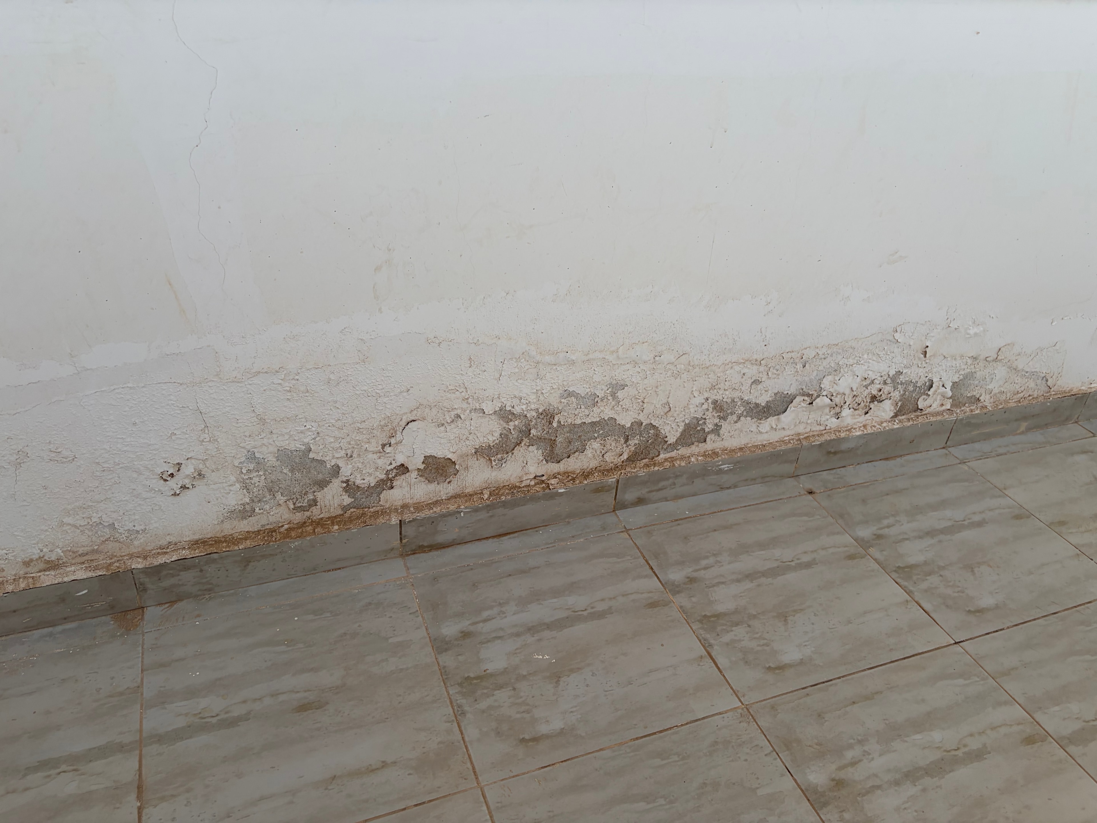 Staircase marble tiles — two different types of marble-effect tile meeting at a step nosing, both heavily stained with brown water marks and general dirt, metal trim strip at nosing, completely neglected