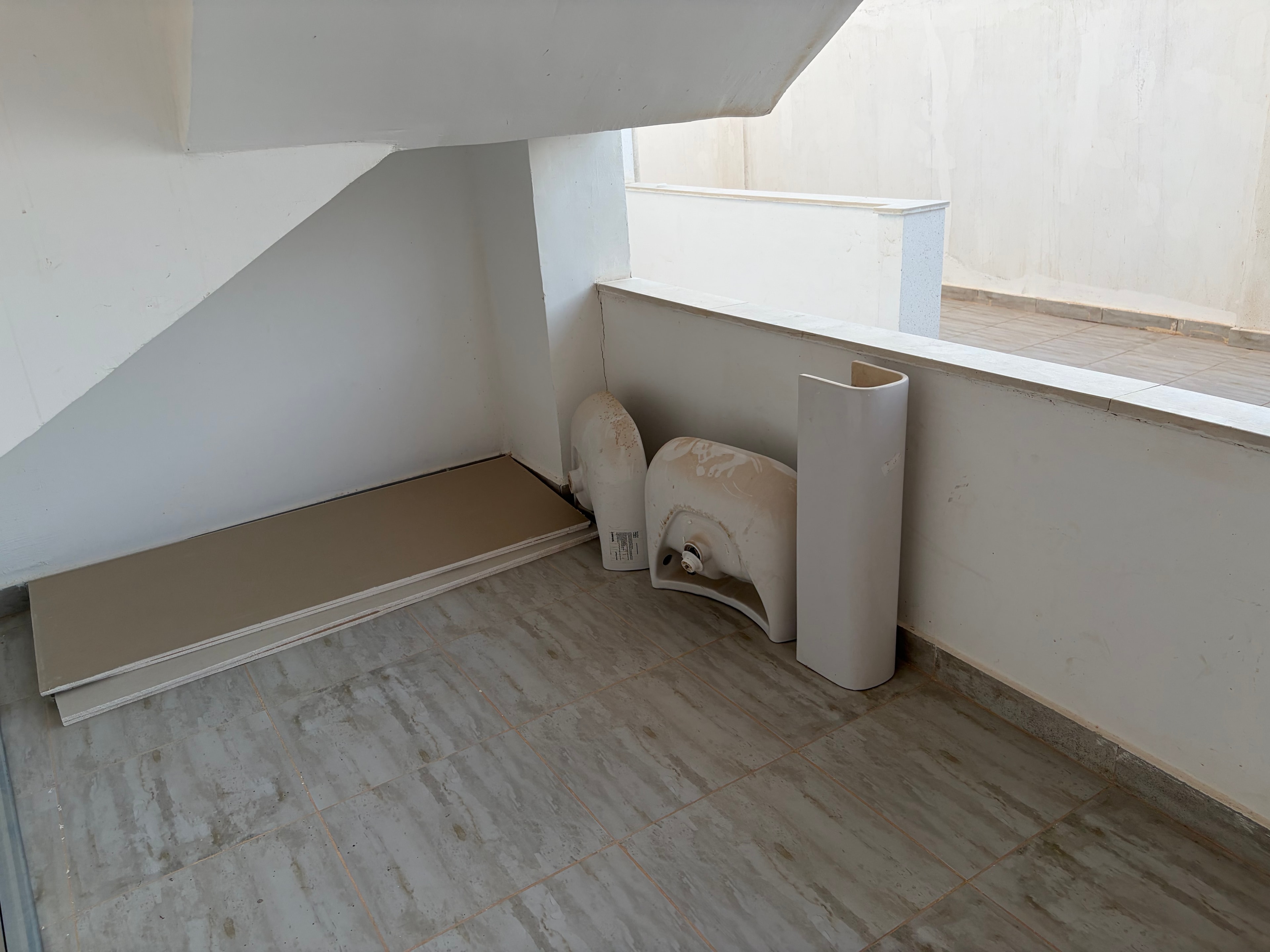 Exposed pipework and loose ceiling panel — bare concrete slab ceiling, large cream pipe/duct with loose end hanging free, plasterboard panel partially detached and hanging at an angle, completely unfinished