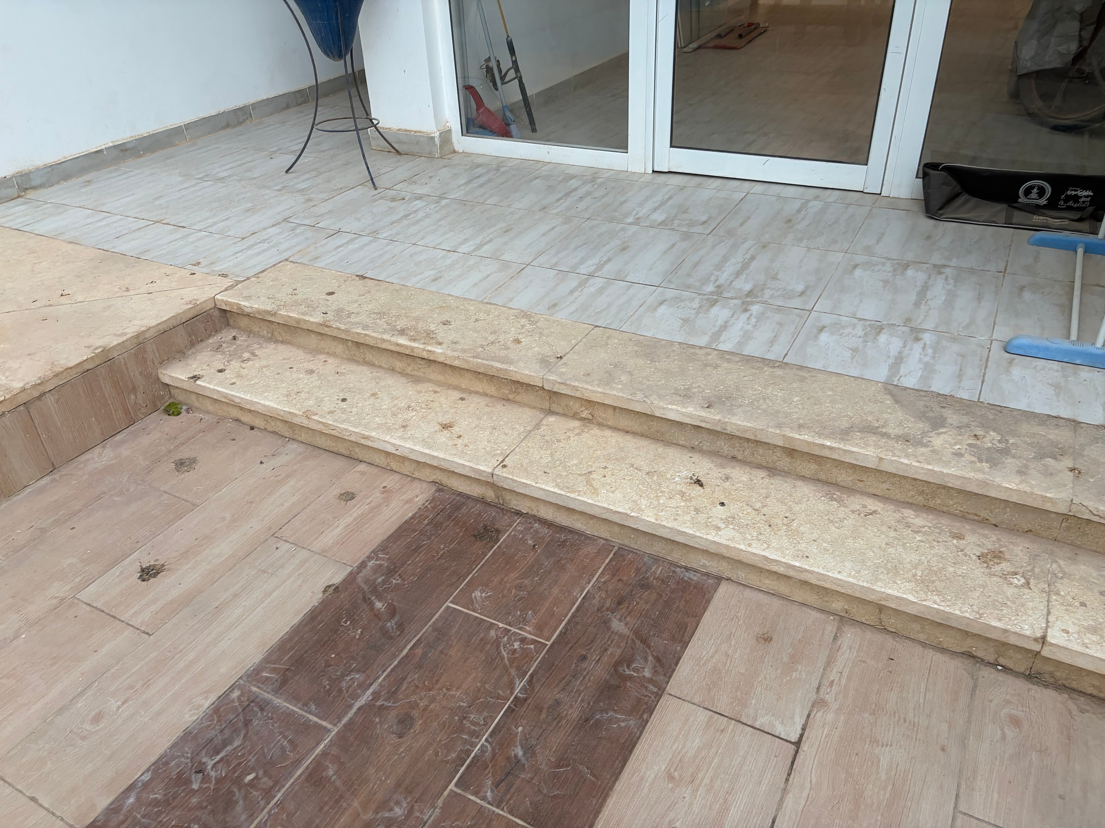 Heavily stained ceiling with mismatched tiles — two completely different tile types meeting mid-ceiling, cornice band heavily stained brown throughout, exposed wiring visible, sliding door below with construction debris