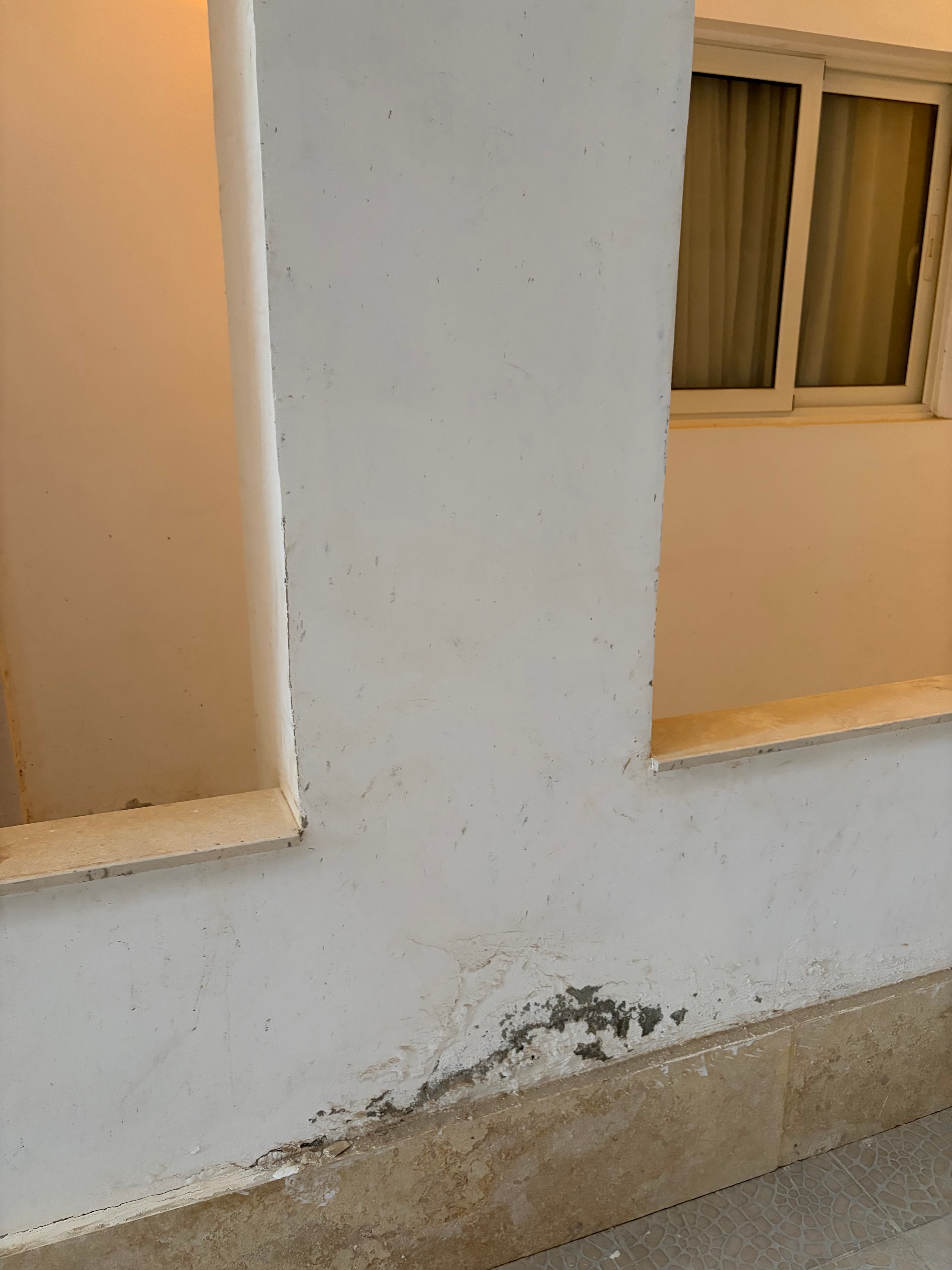 Mould growth at wall/ceiling junction — large patch of black mould at corner where white-painted beam meets tiled wall, surrounding paint dirty and marked, raw timber framing around window opening