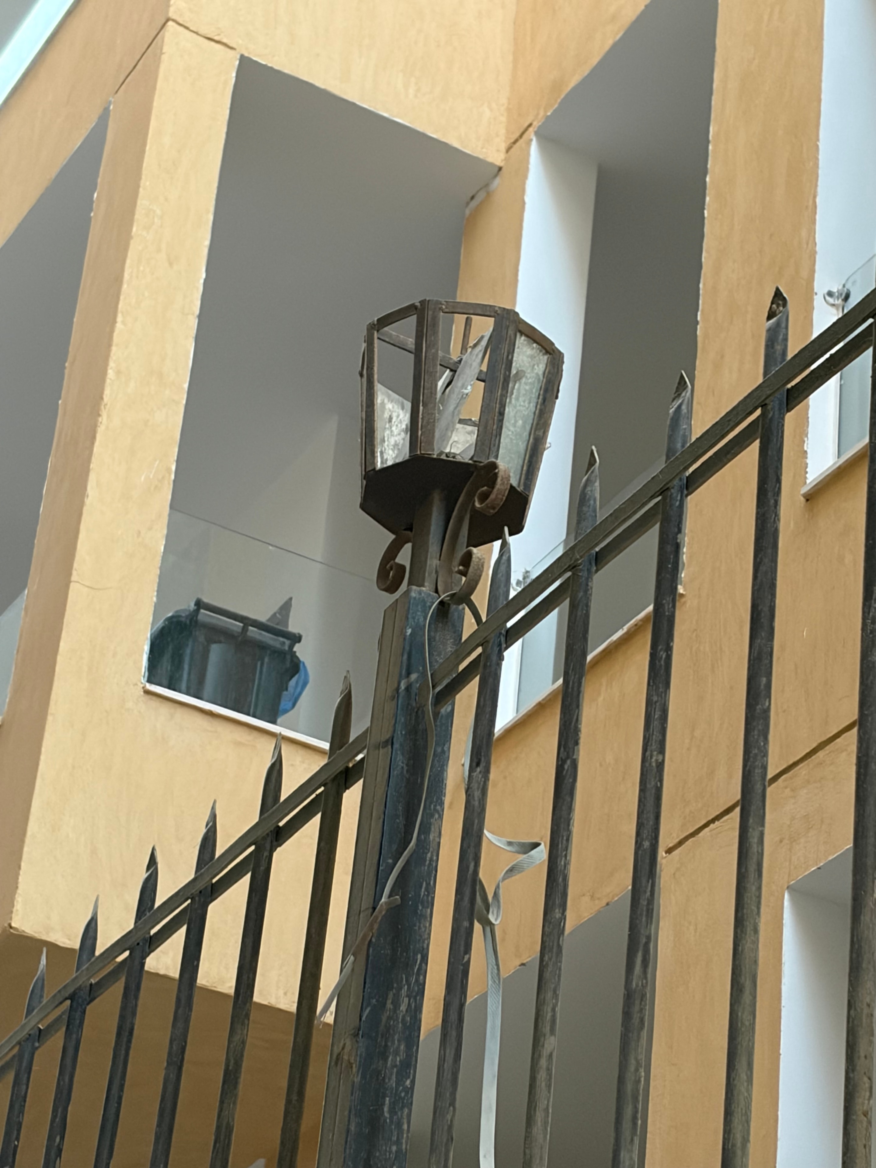Plastic water bottle used as light fitting close-up — clear 1.5-litre bottle with red label wedged upside-down over wall-mounted light bracket, blue pen clip visible — the light fitting in a luxury resort communal area