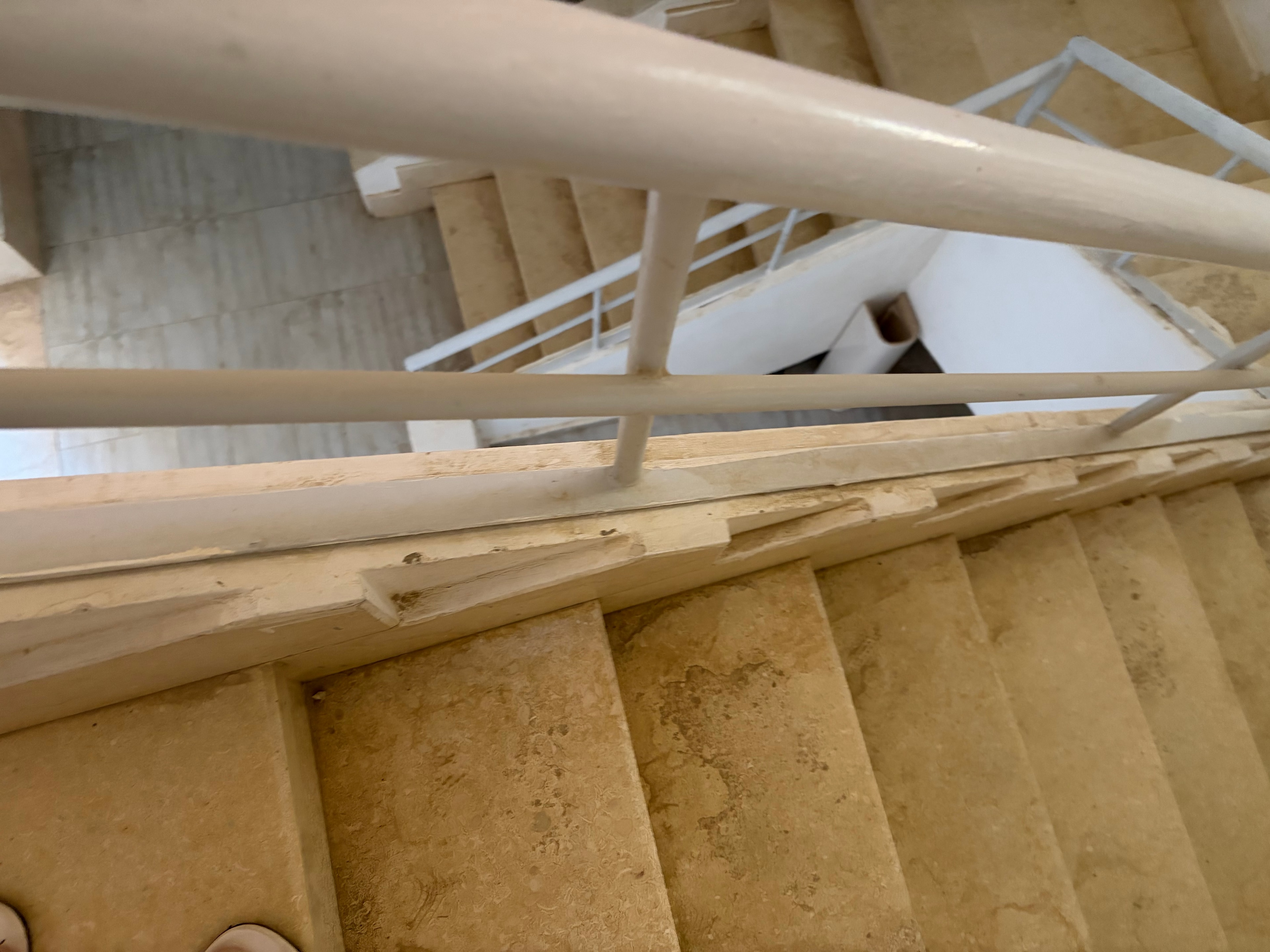 Abandoned toilet pan in communal void space — disconnected toilet sitting on floor with waste pipe stub, loose wiring hanging from ceiling above, copper pipe stub, completely unfinished and open to communal area