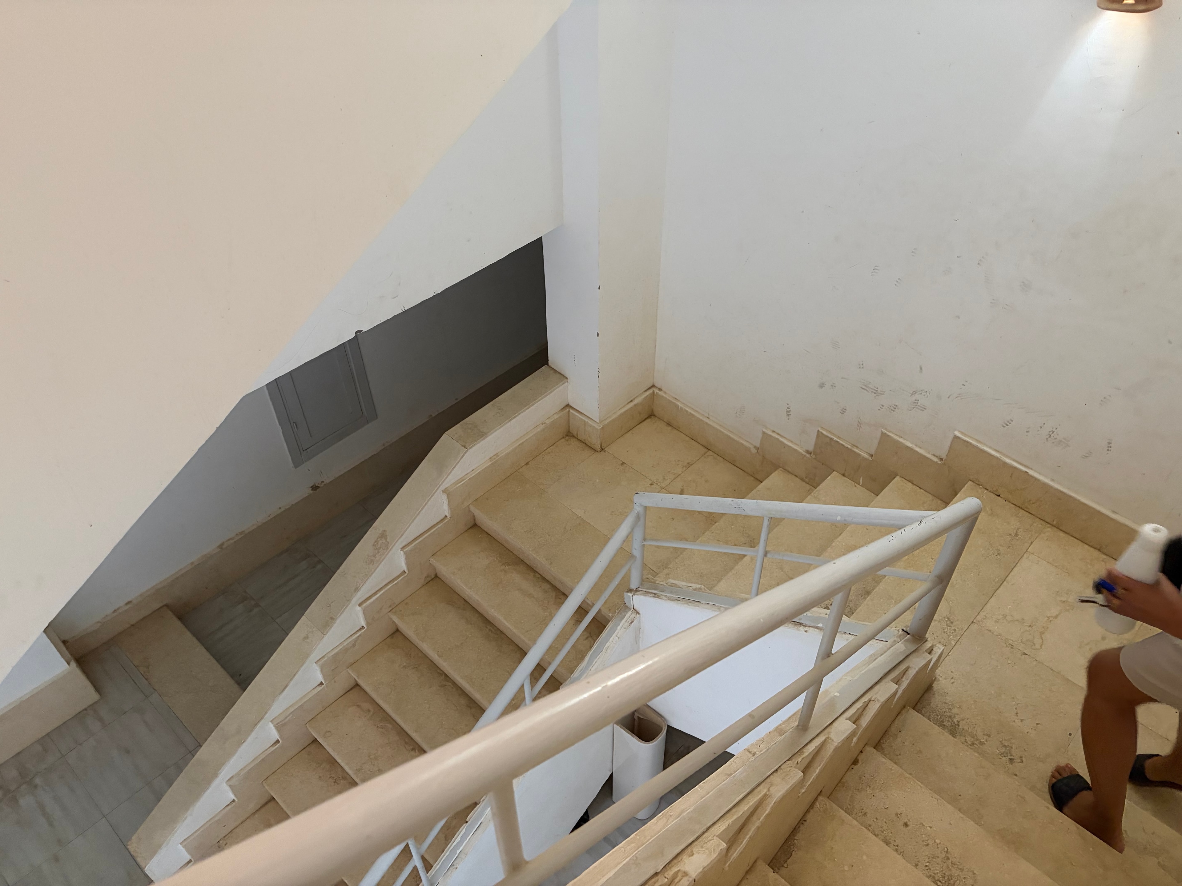 Second corroded cage light fitting in same stairwell — metal completely oxidised and rusted through, identical corroded fitting visible in background, cardboard panels on landing above